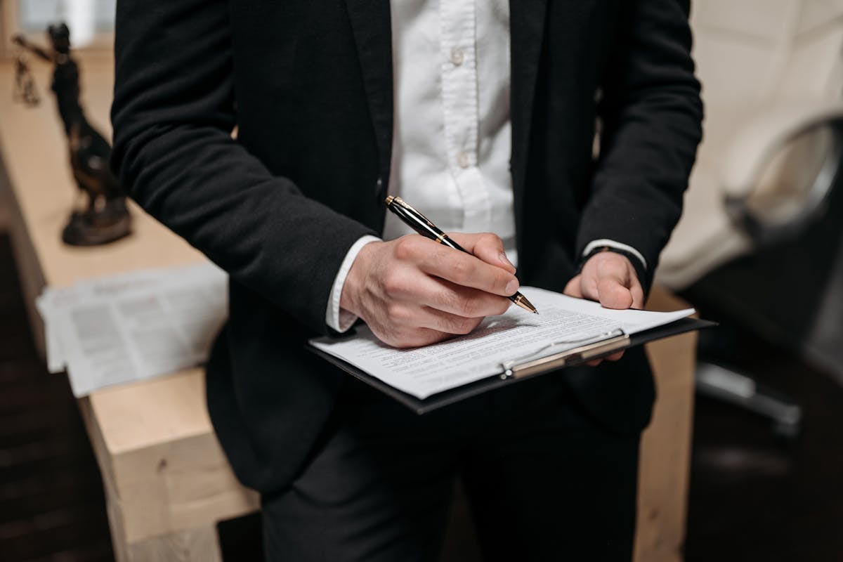 A skip tracing professional in a suit working on a legal case, taking notes while reviewing data on a laptop.